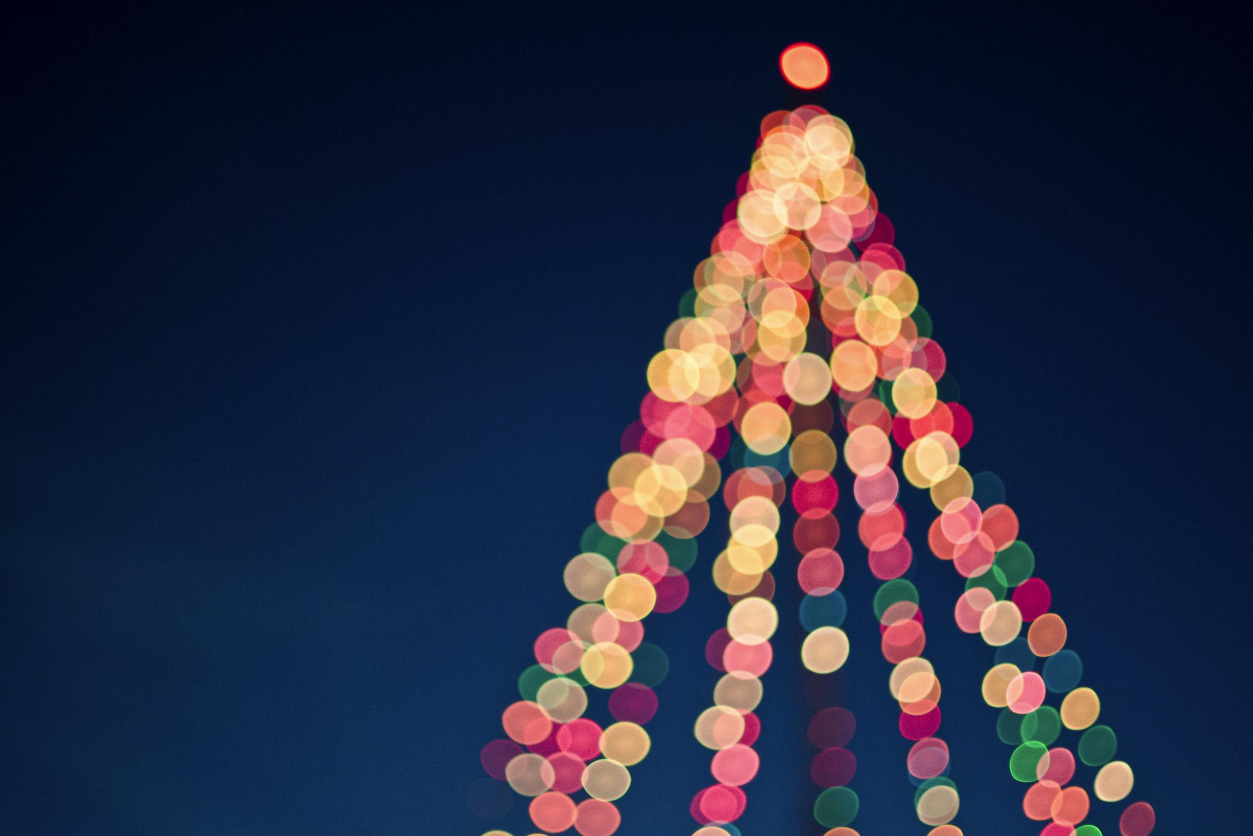 Colorful bokeh lights forming a Christmas tree against a dark blue sky.